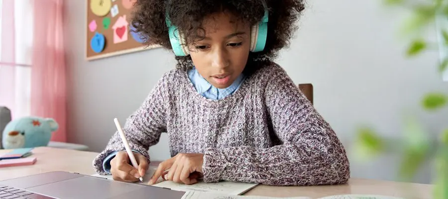 Young girl focused on writing in a notebook at school.
