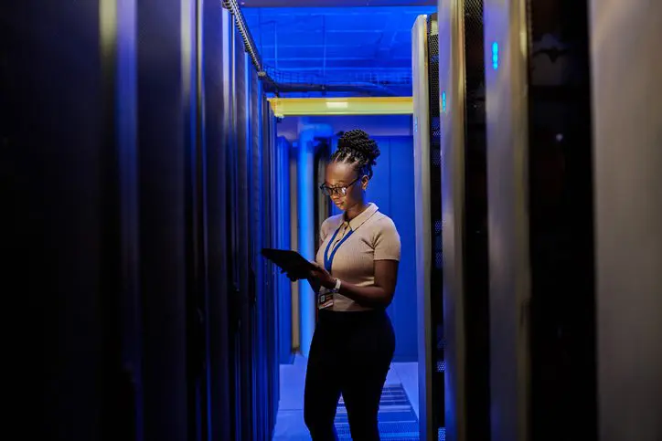Female IT technician monitoring data servers with a tablet.