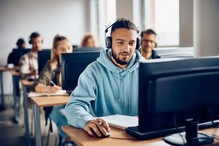 Young man in a hoodie and headset working intently on a desktop computer.