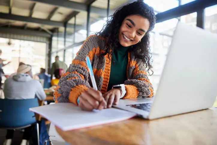 Woman in a striped sweater writing in a notebook at a cafe table.