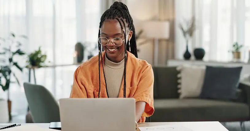 Young woman wearing glasses using a laptop and smiling.
