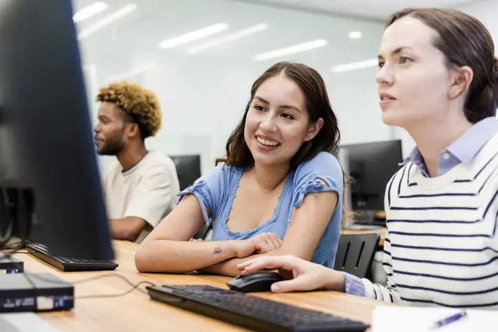 Group of students smiling while seated at desktop computers.