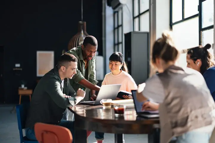 Group of coworkers discussing work around a table in a casual office.