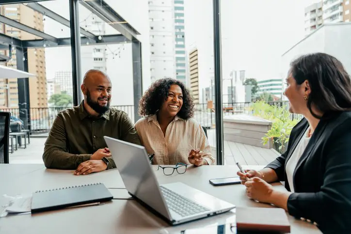 Couple speaking with a businesswoman in a glass office.